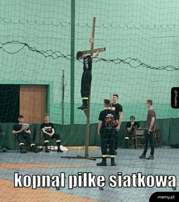 Chłopak stoi na słupie, trzymając się go, podczas meczu siatkówki.