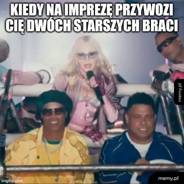 Kobieta z mikrofonem na scenie, dwóch mężczyzn obok niej, wszyscy w okularach przeciwsłonecznych.