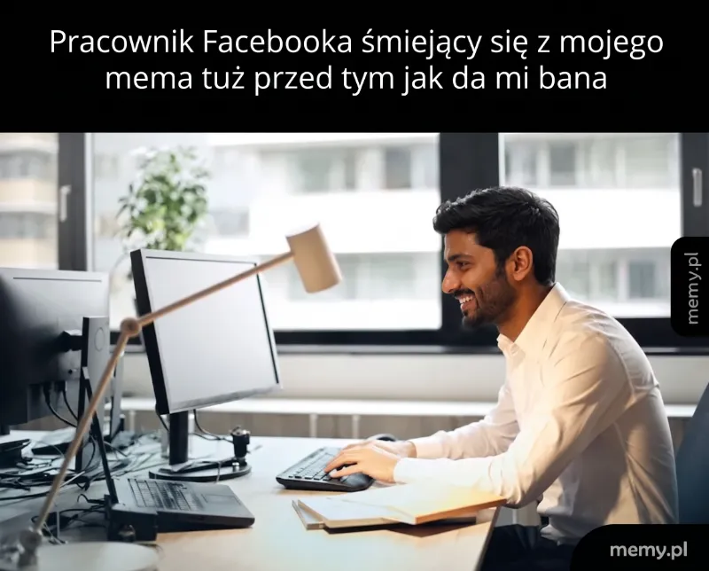 Mężczyzna przy biurku, uśmiechający się podczas pracy na komputerze.