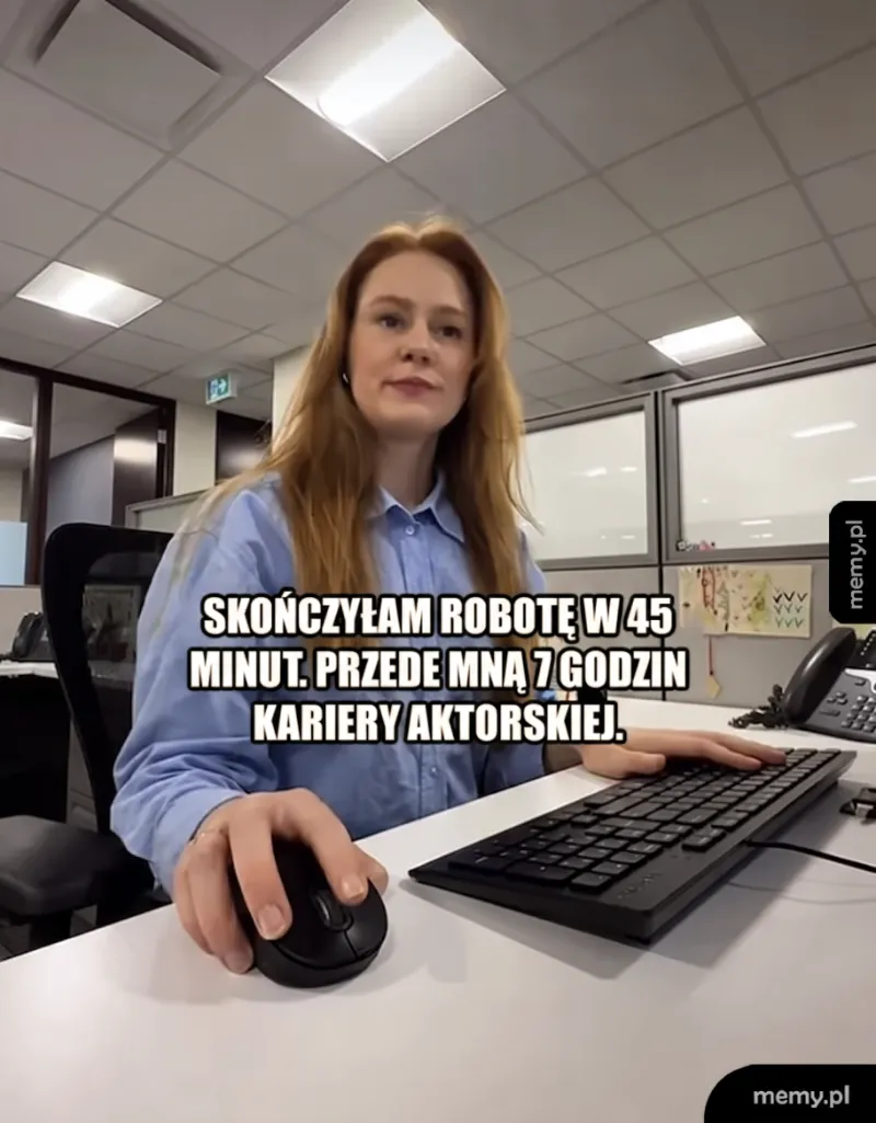 Kobieta w biurze przy komputerze, uśmiechnięta.