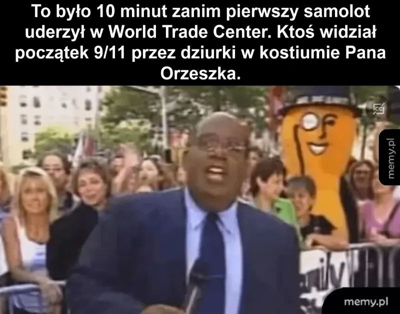 Mężczyzna w garniturze mówi do kamery, w tle tłum ludzi i postać w kostiumie.