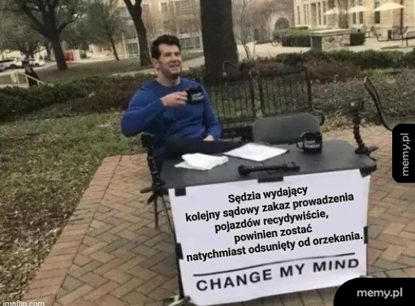 Mężczyzna siedzi przy stole z napisem 'CHANGE MY MIND', trzyma kubek.