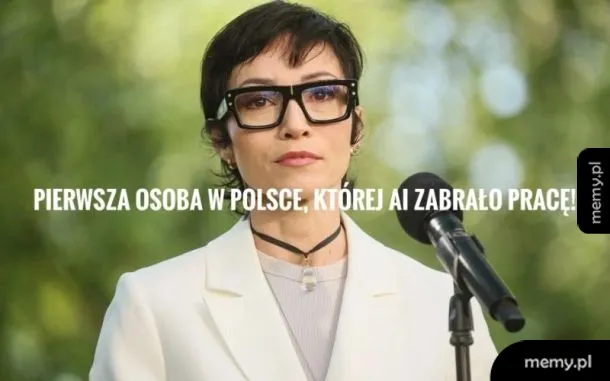 Kobieta w okularach, ubrana w białą marynarkę, przemawia na tle zieleni.