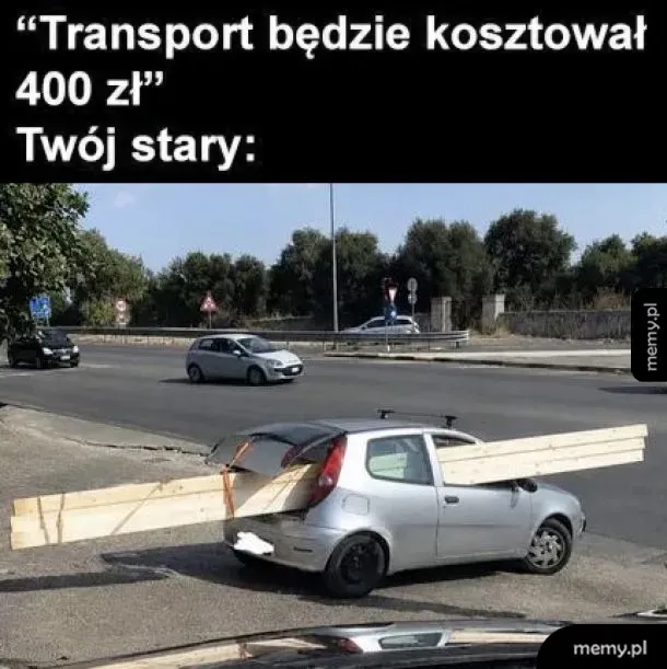 Srebrny hatchback przewożący absurdalnie długie deski wystające z bagażnika i przedniego okna.