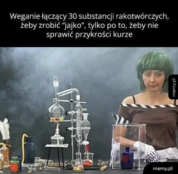Kobieta w zielonej peruce stoi przy skomplikowanej aparaturze chemicznej w stylu laboratorium.