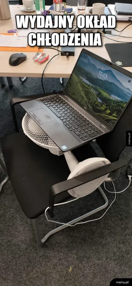 Laptop leżący na włączonym wiatraku biurkowym stojącym na krześle w biurze